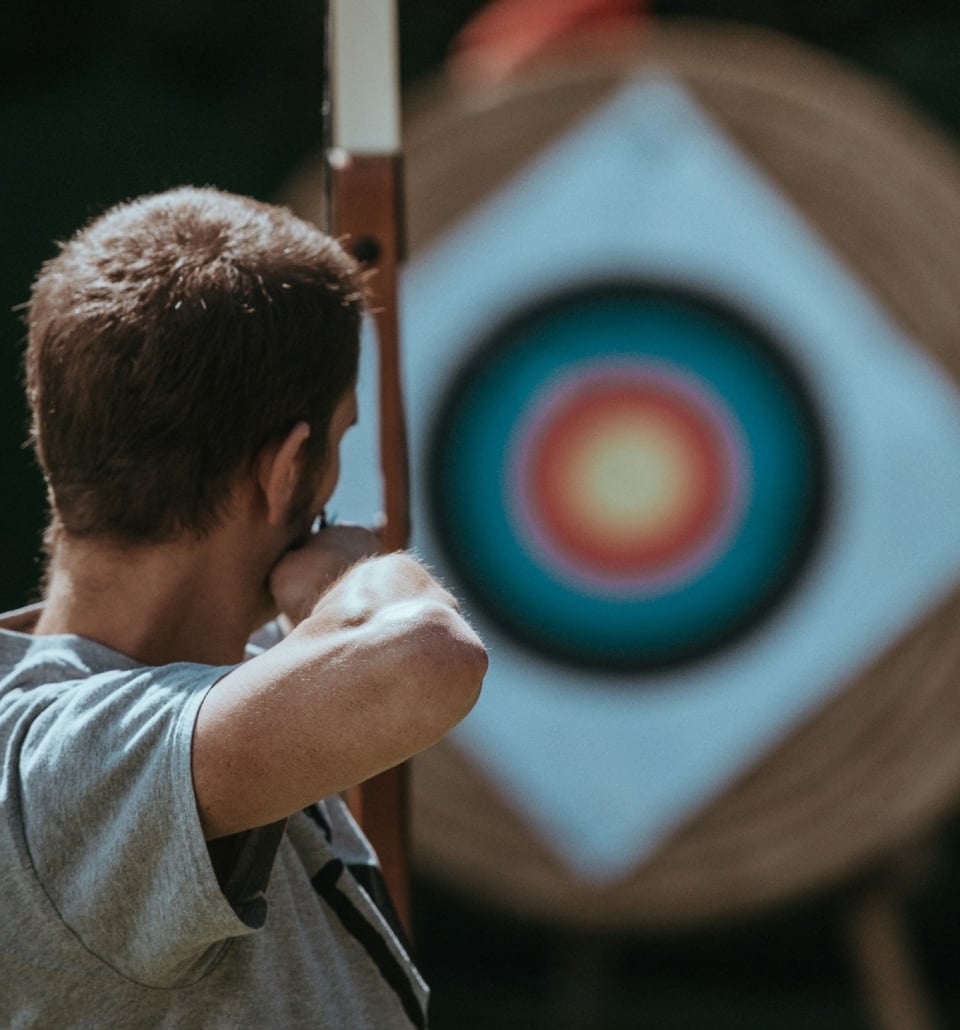 A focused man aiming at an arrow in front of a target.