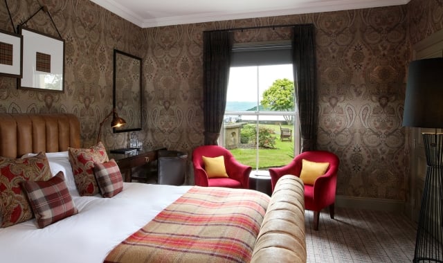 a bed with a night stand beside it and two red chairs in front of a window