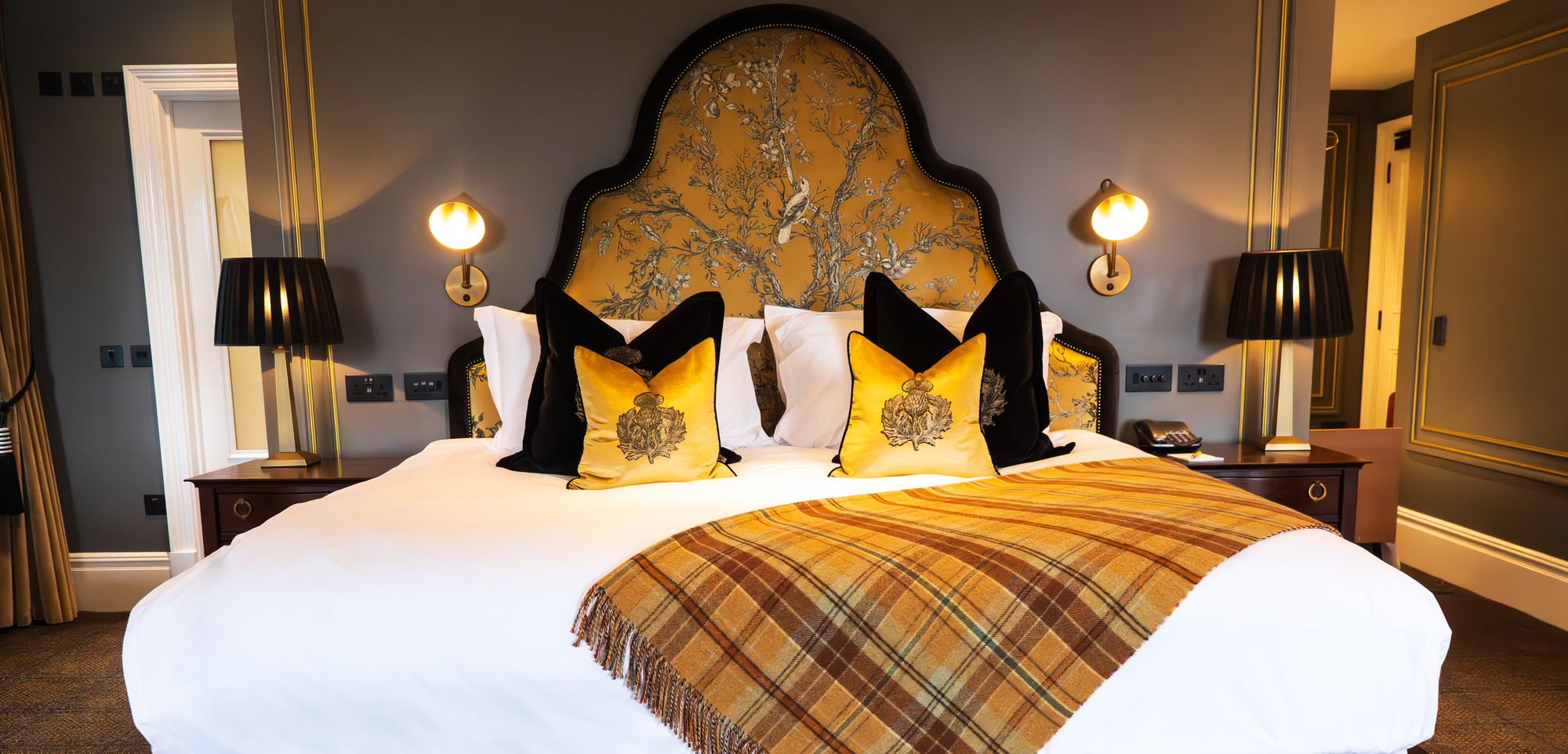 a luxurious bed with a large headboard and tartan blanket