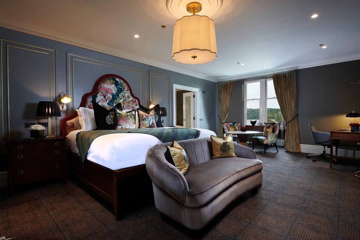 A luxurious suite at Cameron House featuring a bedroom with a bed, sofa, lamp, and table.