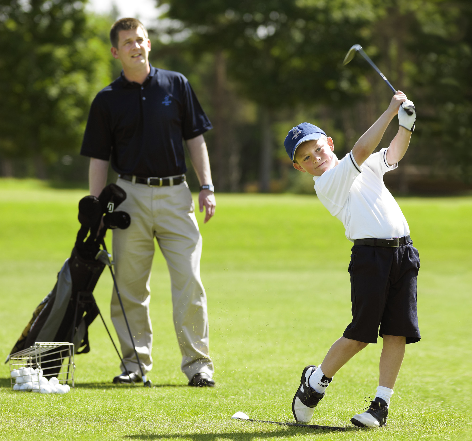 a kid swinging his golf club with his dad looking at him from behind