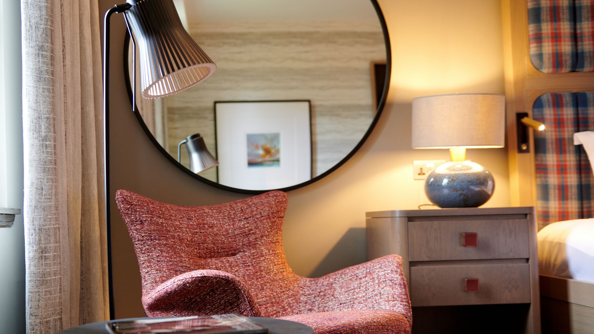 A comfortable hotel room chair with a large mirror above it.