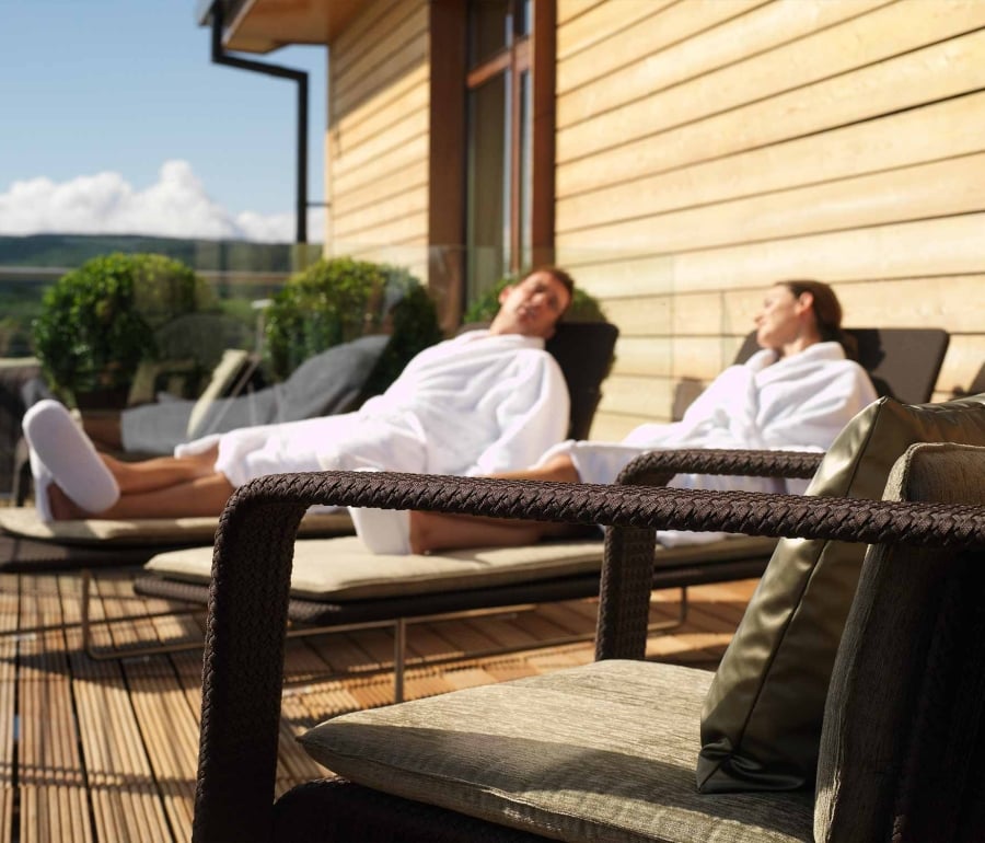 a male and female sitting outside in robes on lounge chairs enjoying the sun