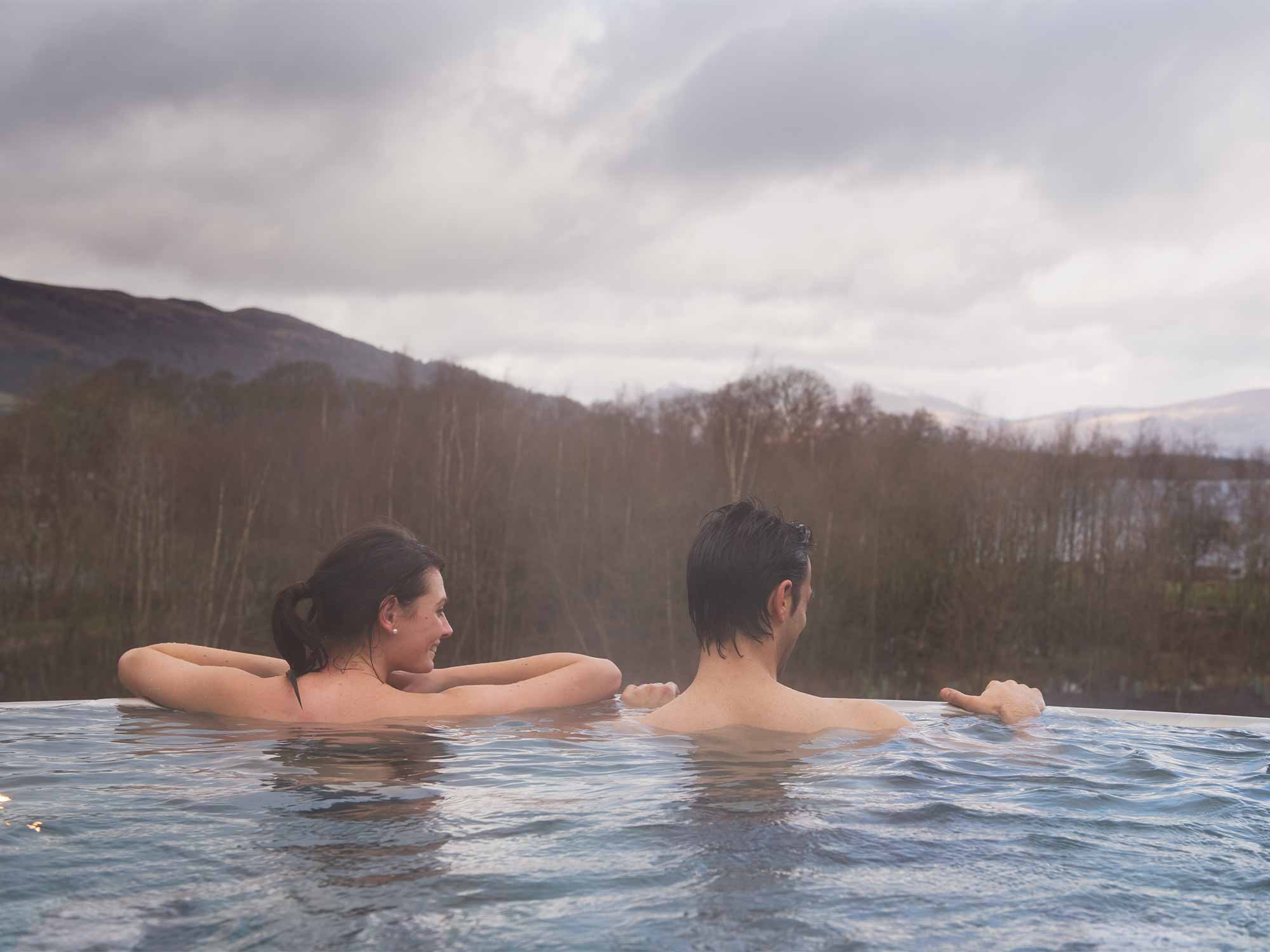 two people in an outdoor infinity pool looking at the forest