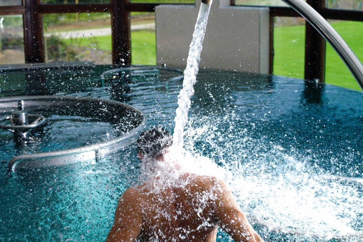 a person sitting in a pool with water flowing into the pool and great views of the outside in the background