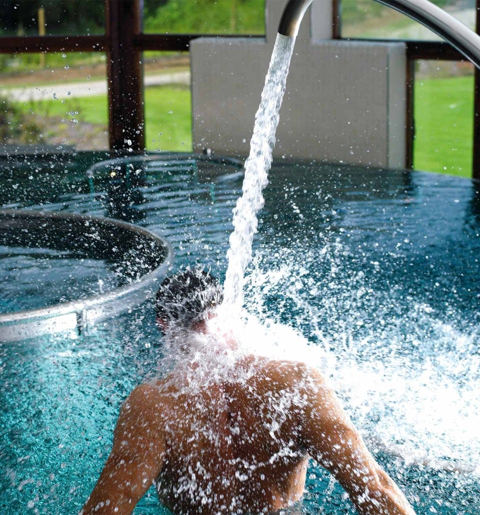 a person sitting in a pool with water flowing into the pool and great views of the outside in the background