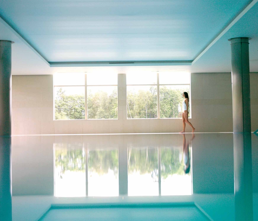 a woman walking along the side of a indoor pool looking outside the window