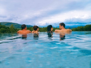 two couples sitting in an out door infinity pool looking over the edge to the forest below