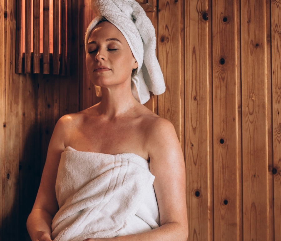 a woman wrapped in a towel and a towel on her head relaxing in a sauna