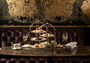 some small finger foods with a tea pot and glasses of champagne on a table with a brown leather coach behind