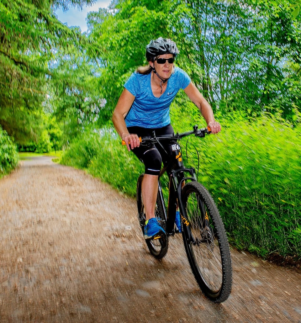 woman riding a bike outside down a dirt trail with green bushes around her