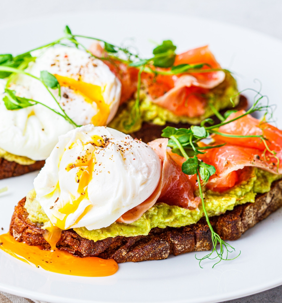 two pieces of toast with avocado spread, sliced meat and eggs