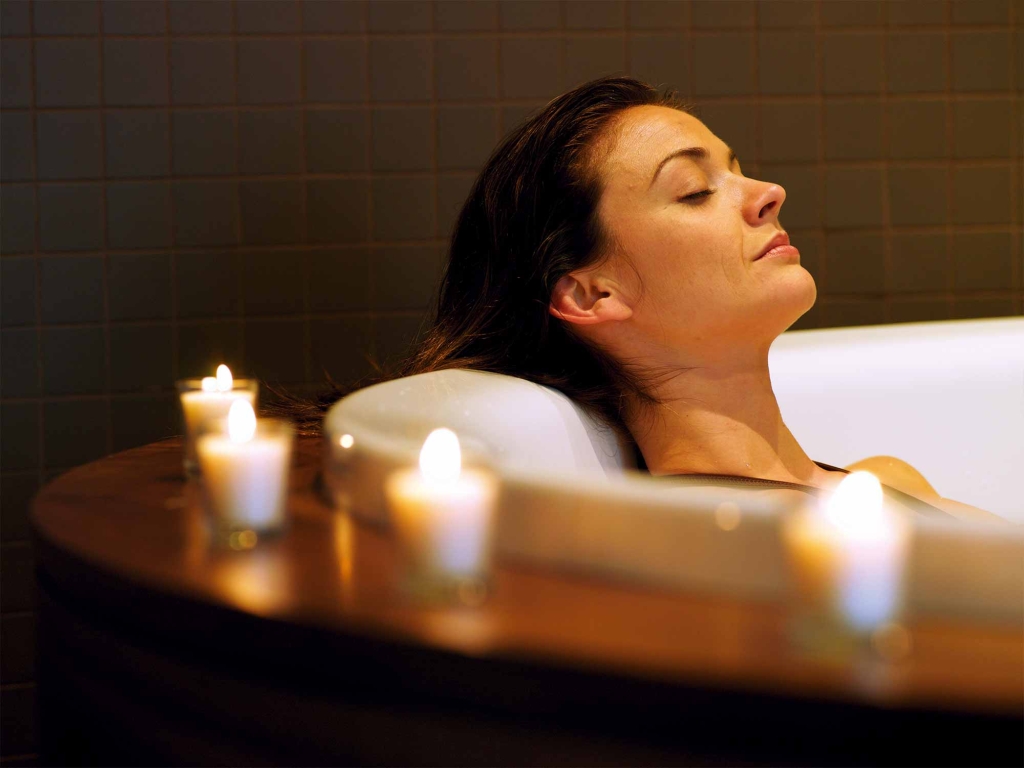 a woman relaxing in a tub with candles lit around her