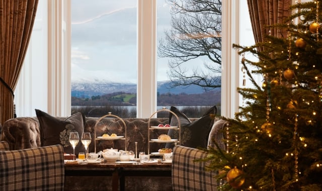 Festive Christmas tree in front of a sofa and afternoon tea setup, framed by a window revealing Loch Lomond.