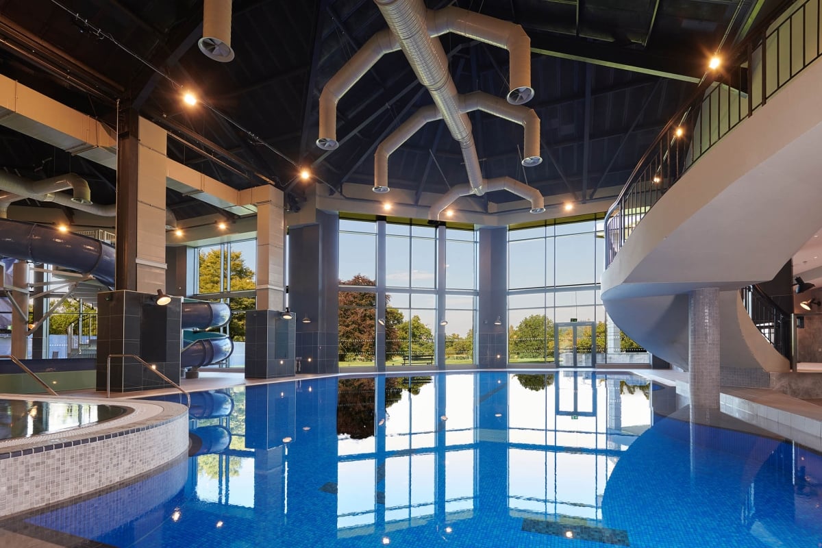 large in door pool with water slides to the side and windows showing the trees out side