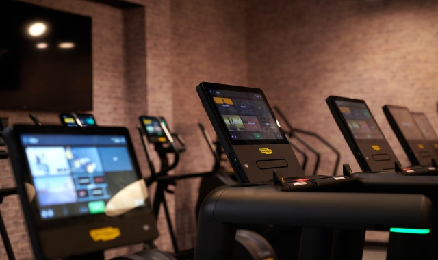 close up view of screens on treadmills with other cardio equipment in the back