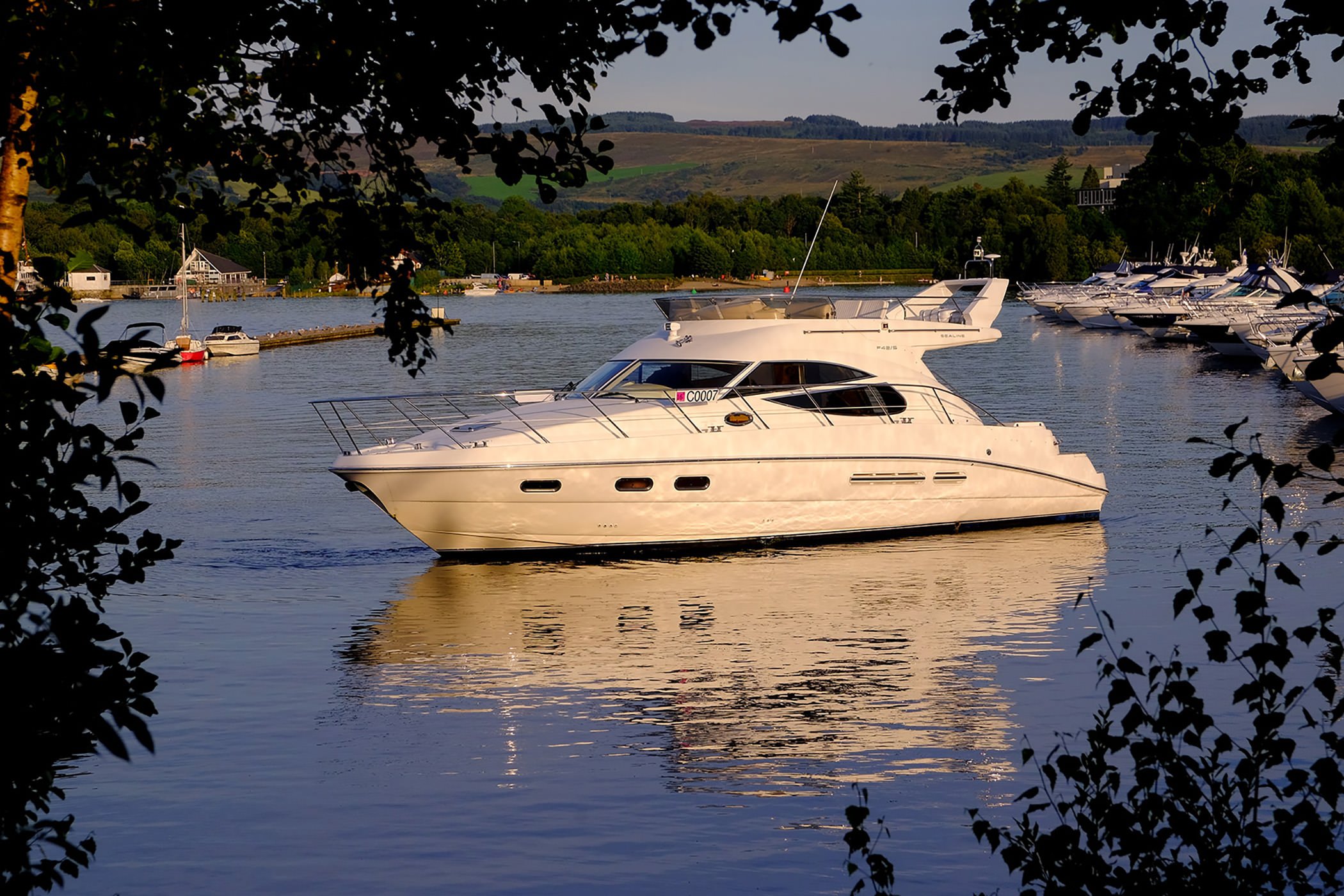 large white boat on the water in a marina on a sunny day with mountains in the background