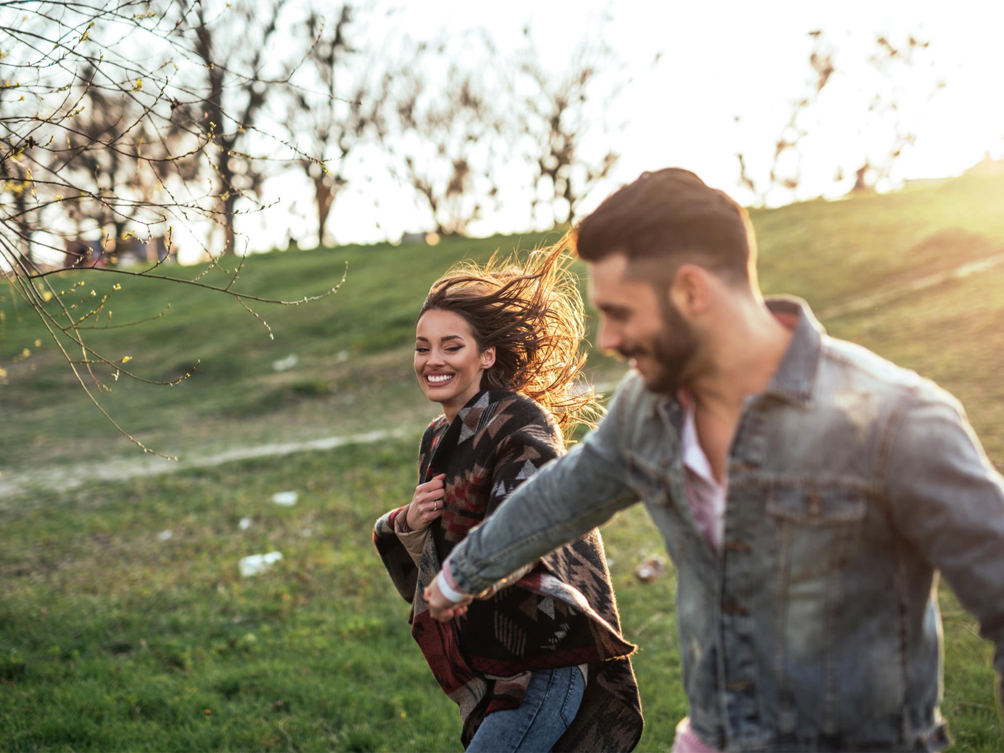 a man and woman holding hands walking through the grass down a hill