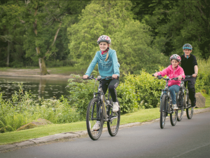 two girls and a man riding their bikes down a trail beside a lake