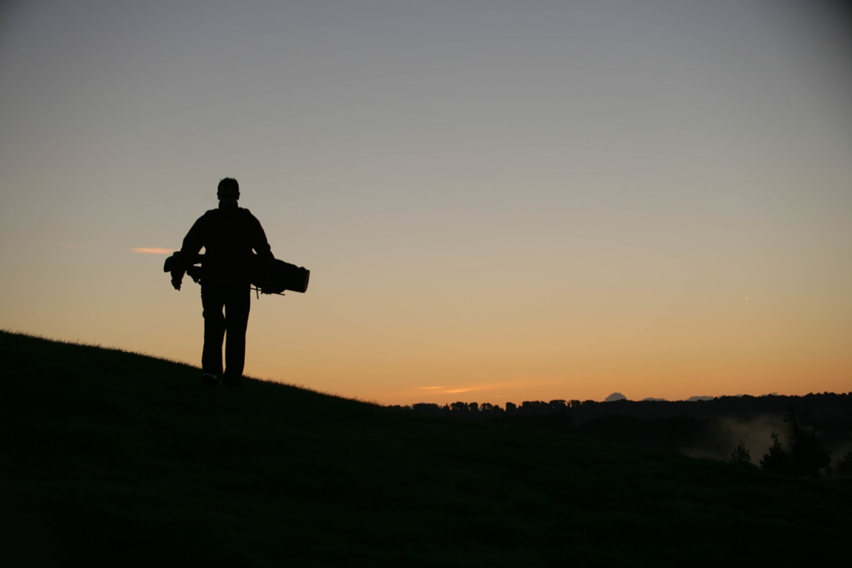 a golfer holding his bag of clubs while watching the sun set