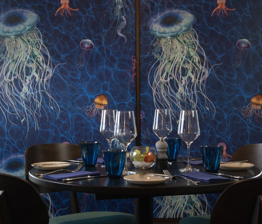 A table with four chairs against a blue wall with painted jellyfish at La Vista restaurant.