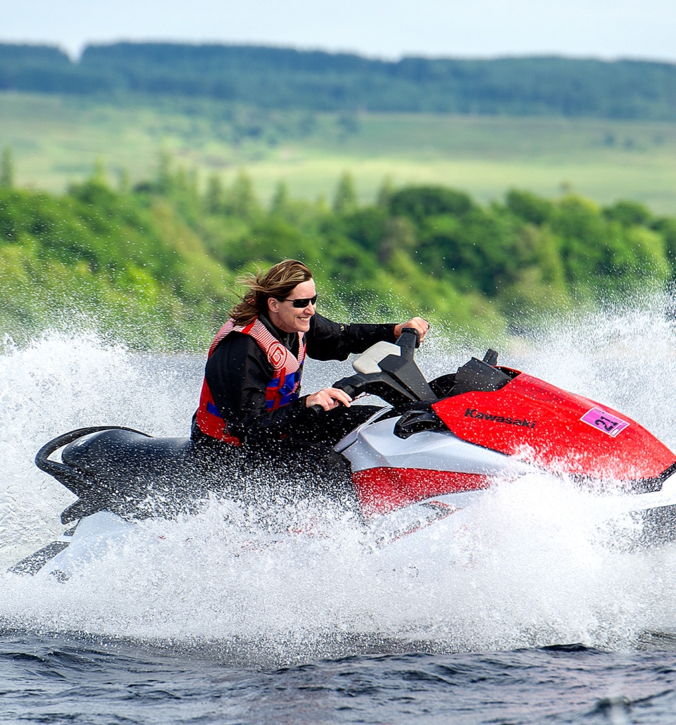 a person riding on a jet ski on the water with a beautiful green forest in the back ground