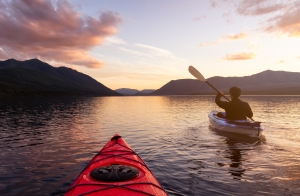 A man paddling a kayak on Loch Lomond at sunset.