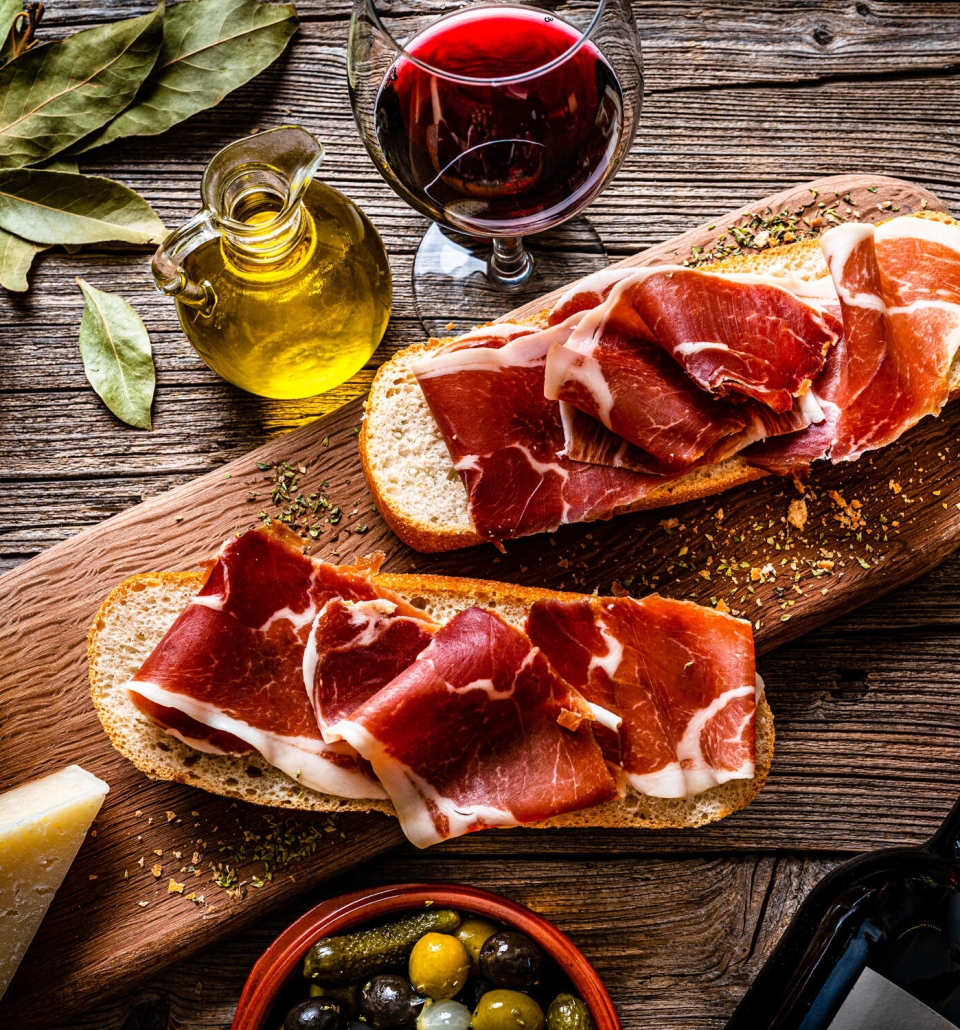 freshly sliced meat sitting on bread with a glass of wine and a bottle of oil