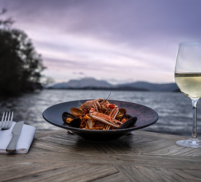 a beautiful seafood dish sitting next to silverware and champagne out doors in front of the water