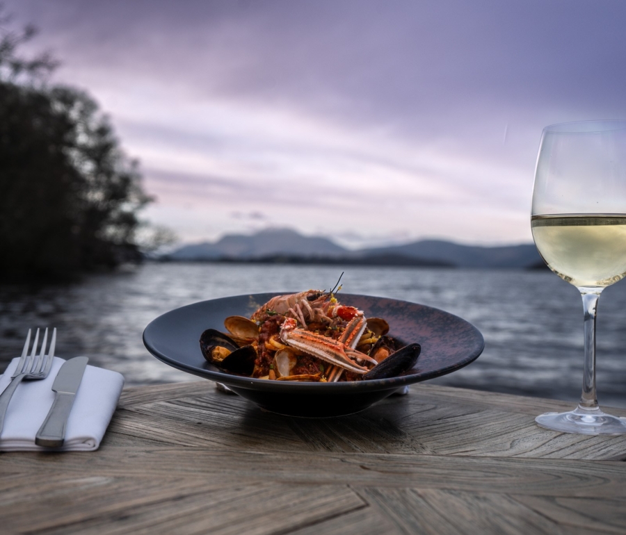 a beautiful seafood dish sitting next to silverware and champagne out doors in front of the water