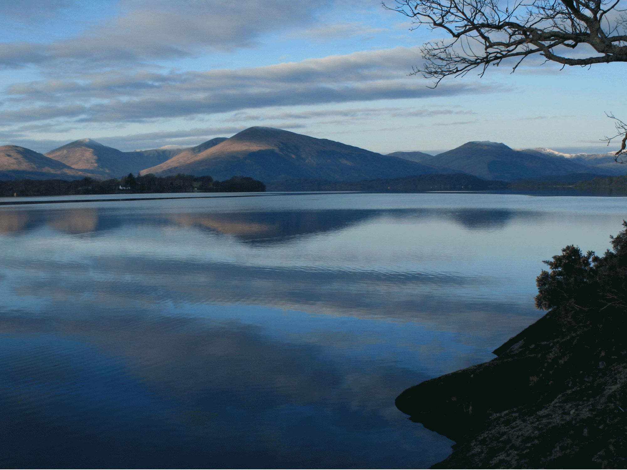 a body of water with mountains in the back ground on a cloudy night