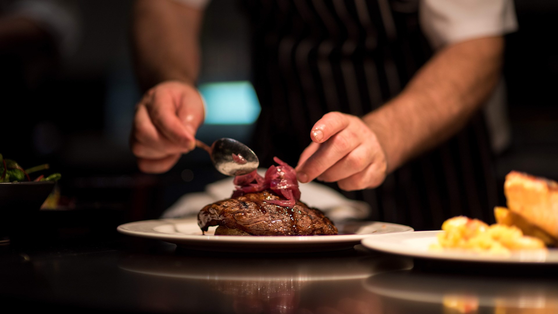 a chef preparing a piece of meat by placing garnish on the top