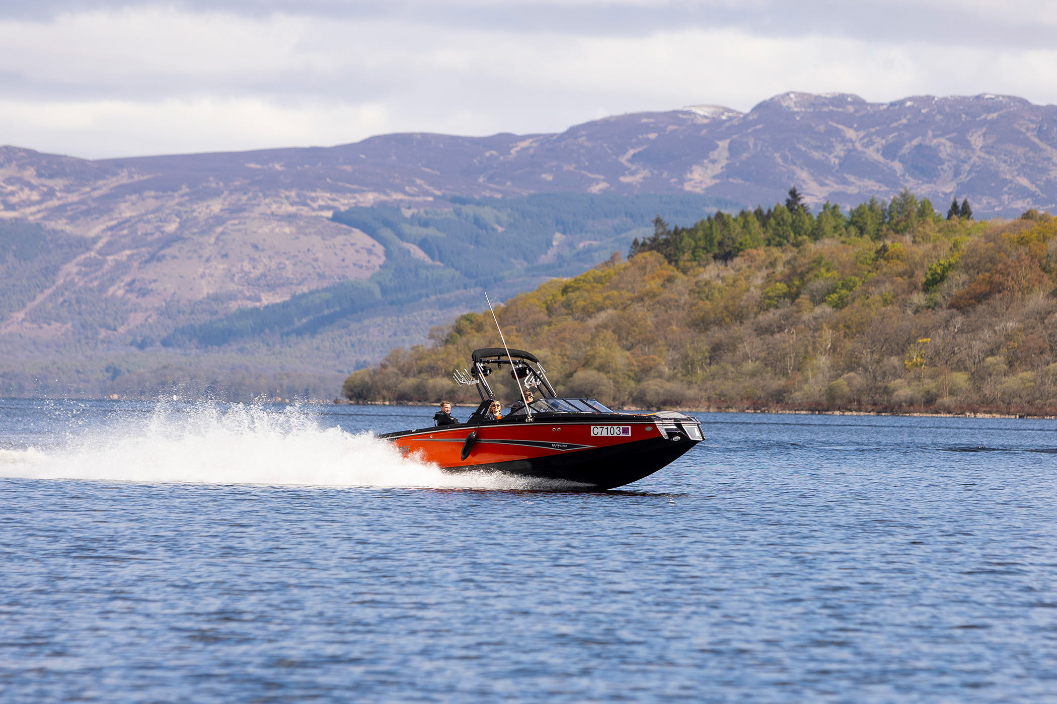 people riding on a red and black boat in the middle of the water with mountains in the background