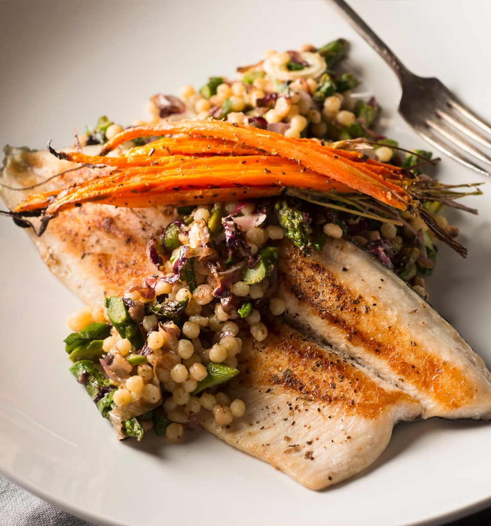 fish sitting under a bed of vegetables on a plate