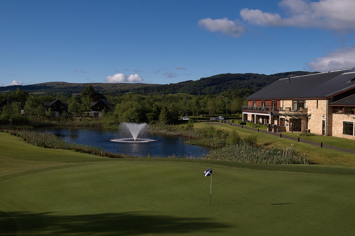 a golf course in front of a pond with a fountain next to a building