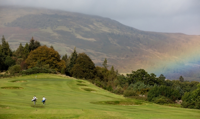 golfers playing golf on a golf course with a rainbow in the back ground