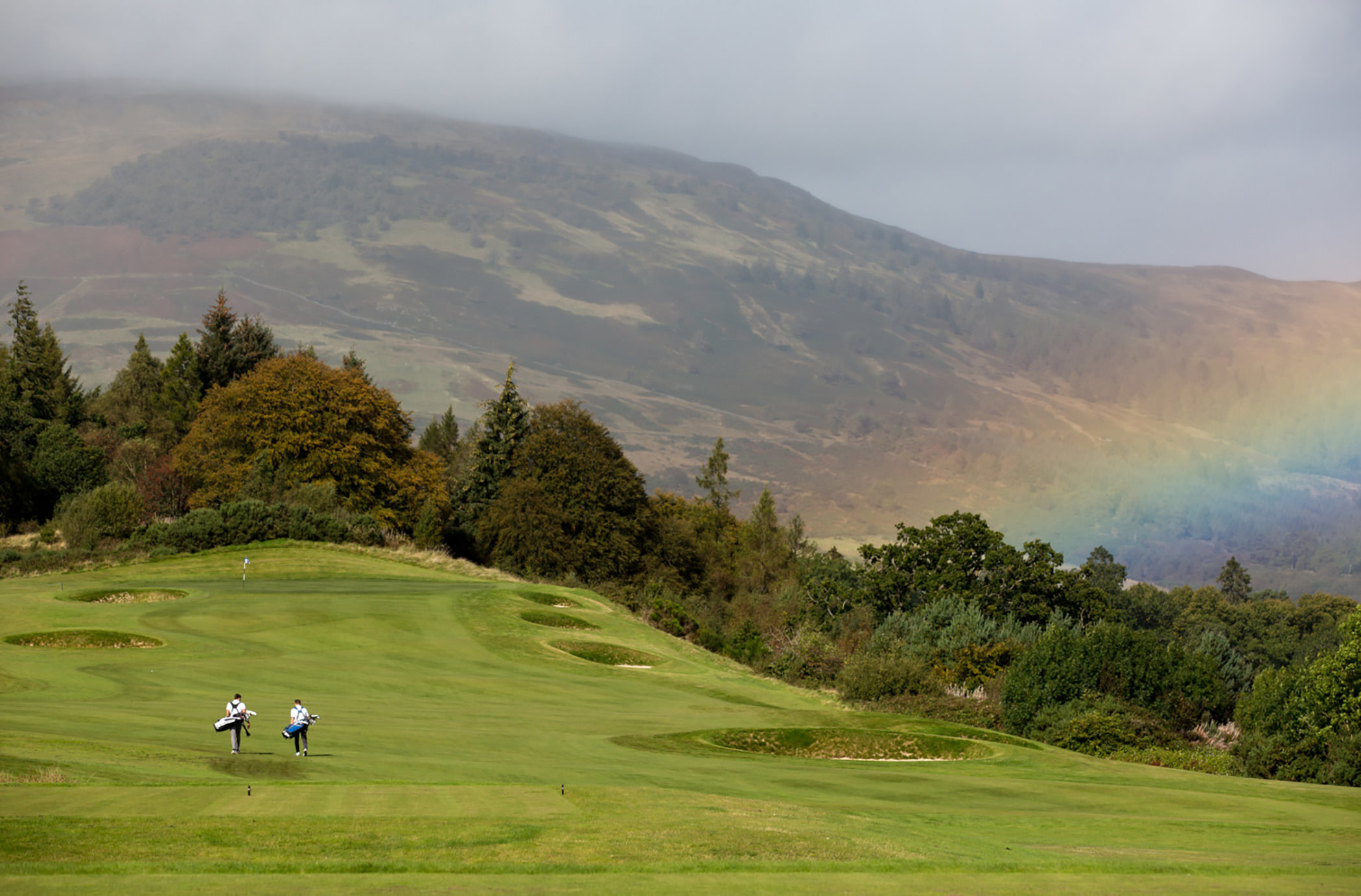 golfers playing golf on a golf course with a rainbow in the back ground