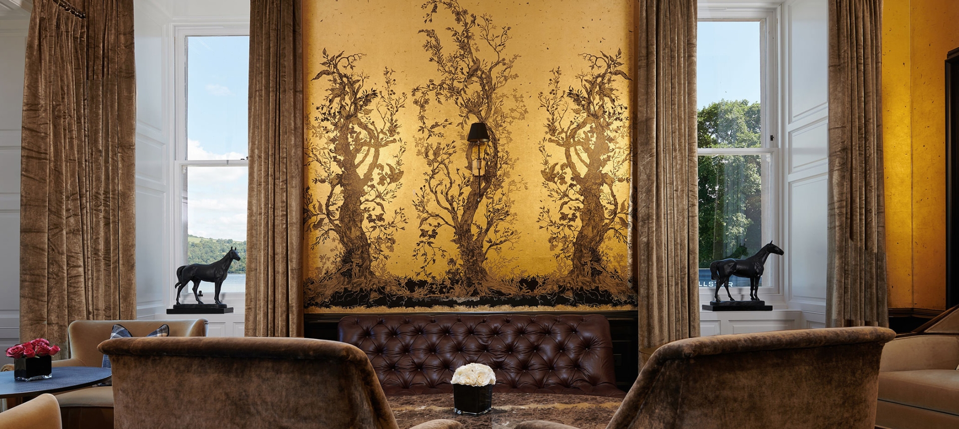 table side view of trees pained onto a wall and large windows looking into the exterior and small horse statues