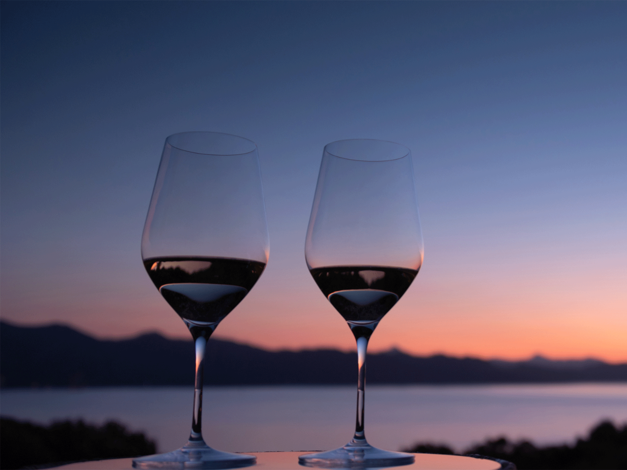 two glasses sitting on a table with the sun setting in the back ground