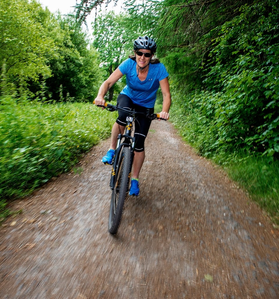 a woman riding her bike down a trail with trees and bushes around her
