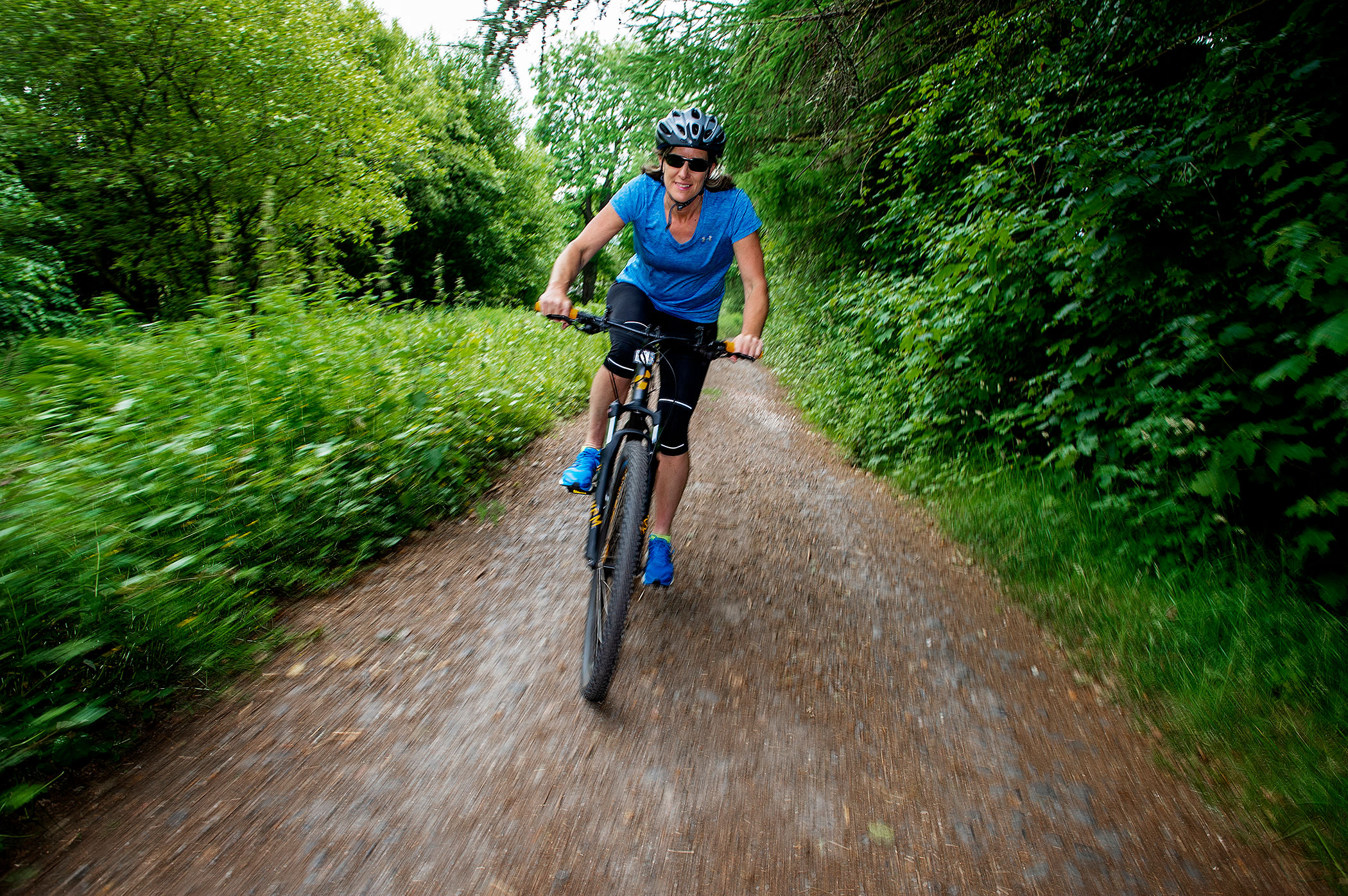 a woman riding her bike down a trail with trees and bushes around her