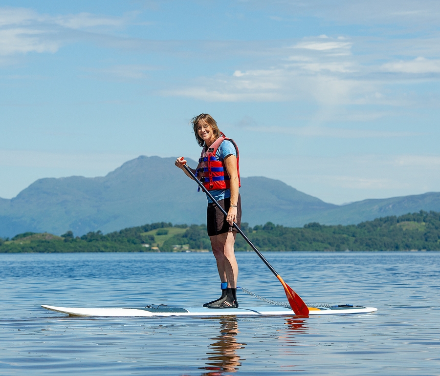 a woman riding on a paddle boat with bright green trees and mountains in the background