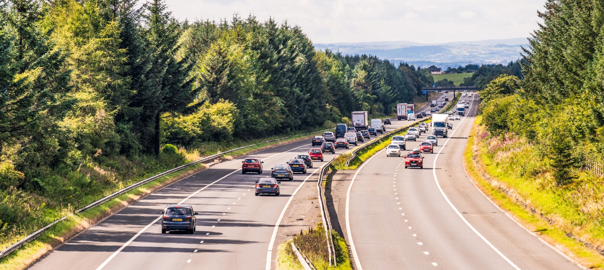 Cars driving on highway with trees and grass.