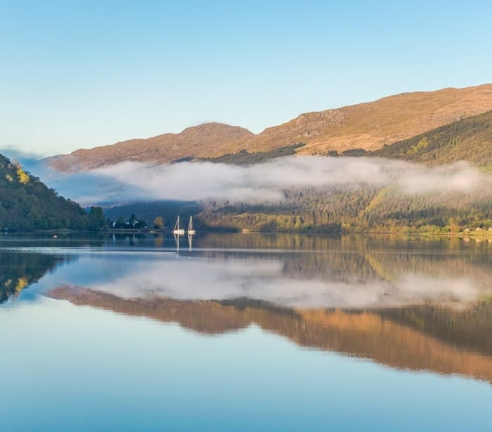 A Scottish loch surround by hills during a sunny day.