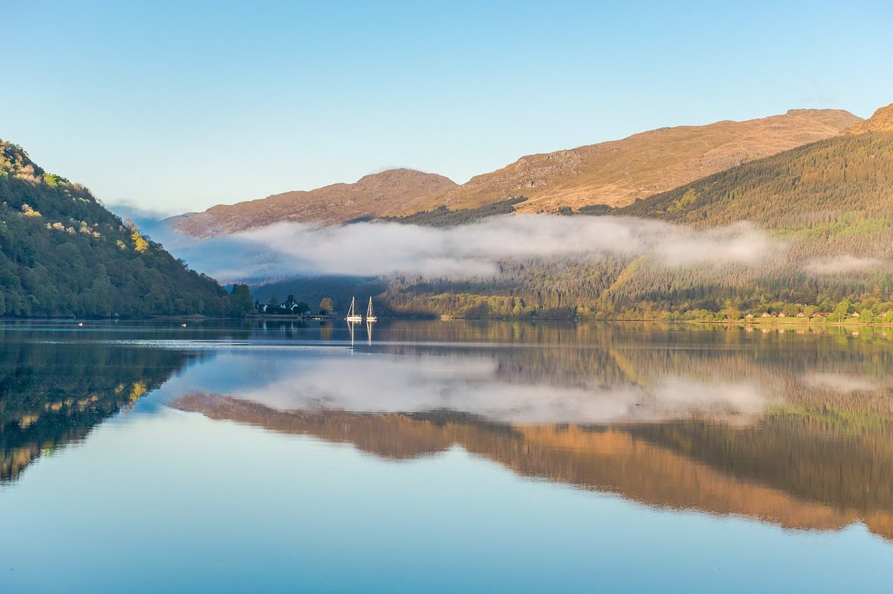 A Scottish loch surround by hills during a sunny day.